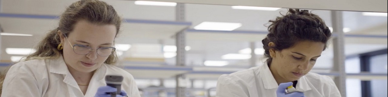 ventures-blog-hero-2000x500.jpg：两名女性穿着白色实验室工作服，一名女性正在使用显微镜